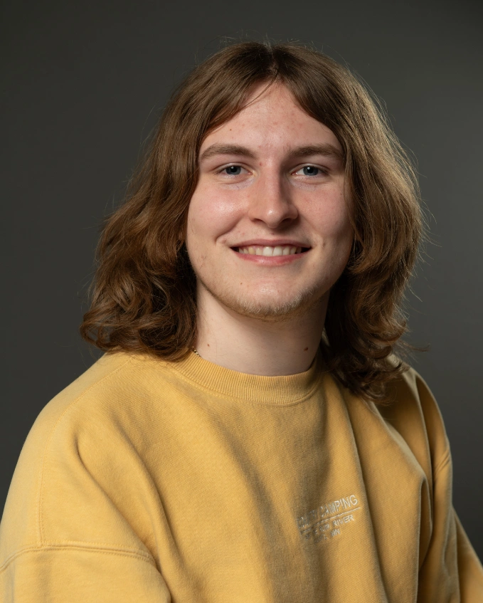 charlie rundquist posing for a headshot, smiling and wearing a yellow sweater